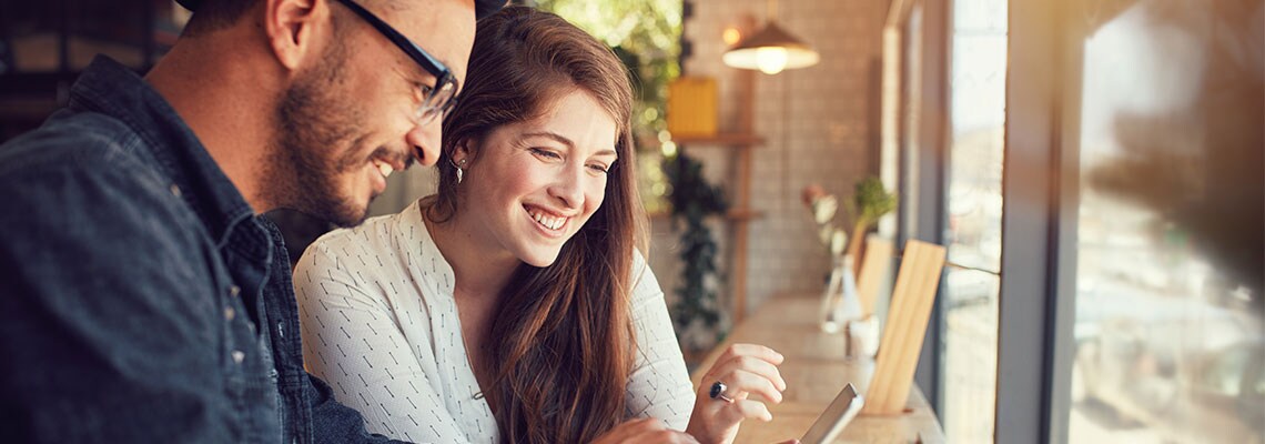 Couple enjoying a coffee shop looking at a tablet while staying at an Aiden hotel
